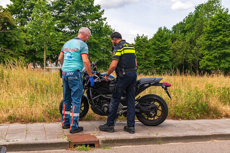 Een agent en ambulanceverpleegkundige bekijken de schade aan de motorfiets. - Foto: Peter Denekamp