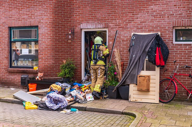 Brandweermannen halen rotzooi uit de hal om de gaskraan dicht te draaien. - Foto: Peter Denekamp