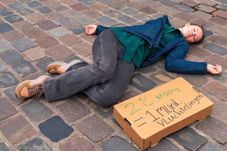 Een klimaatactiviste ligt 'dood' op de keien van de Grote Markt tijdens het luchtalarm. - Foto: Peter Denekamp