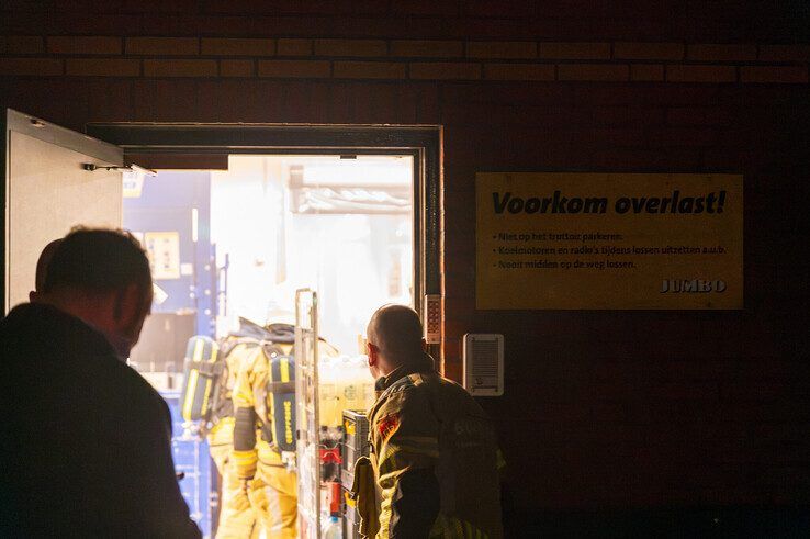 Brandweerlieden gaan de 'rokerige' supermarkt binnen op zoek naar de oorzaak. - Foto: Peter Denekamp