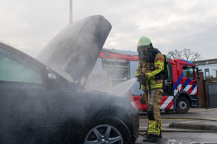 Een brandweerman blust de autobrand op de parkeerplaats van de supermarkt. - Foto: Peter Denekamp