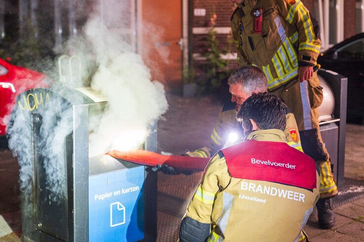 Brandweerlieden blussen de brand in de ondergrondse papiercontainer. - Foto: Peter Denekamp