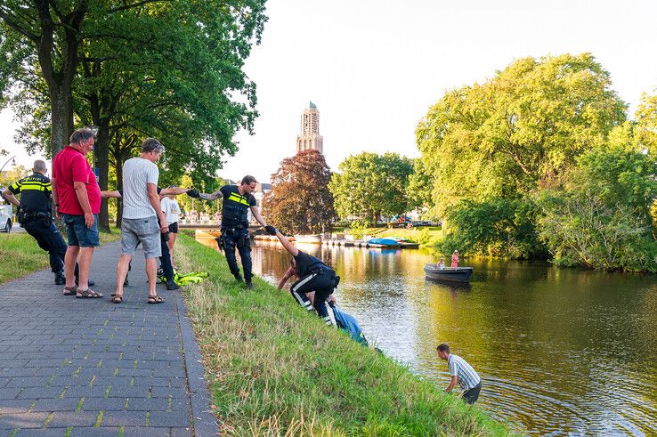 Omstanders en agenten trekken de drenkeling tegen de steile walkant omhoog. - Foto: Peter Denekamp