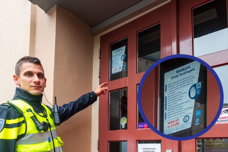 Politieman Nikos Giannos wijst naar de sticker op de deur van een deelnemende horecazaak. - Foto: Peter Denekamp