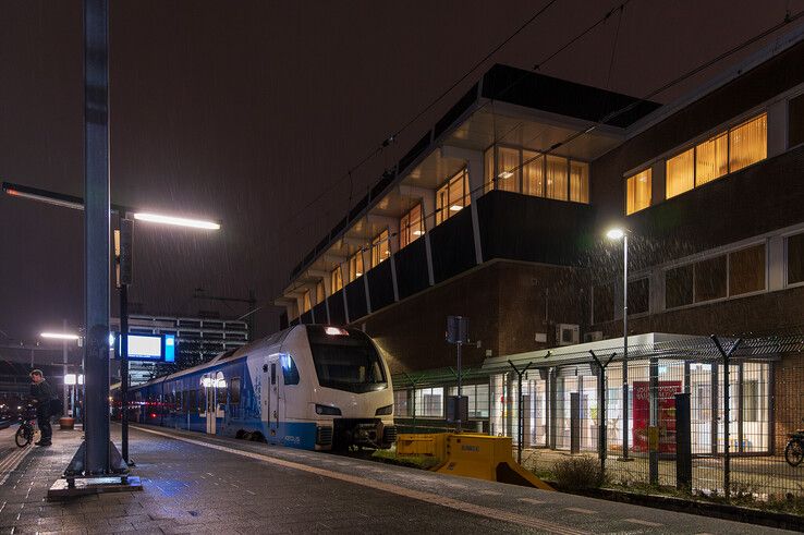 Een eenzame reiziger wacht in alle vroegte op de trein naar Kampen, op de achtergrond verkeersleidingspost Zwolle. - Foto: Peter Denekamp