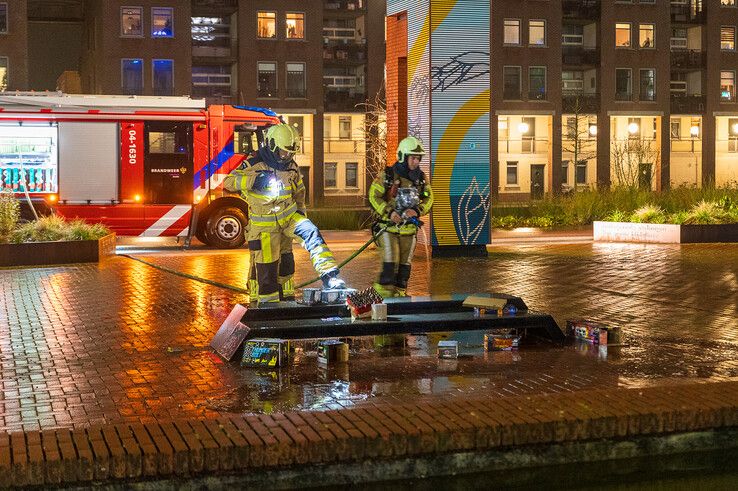 Brandweerlieden blussen het vuurwerkafval op het Lübeckplein. - Foto: Peter Denekamp