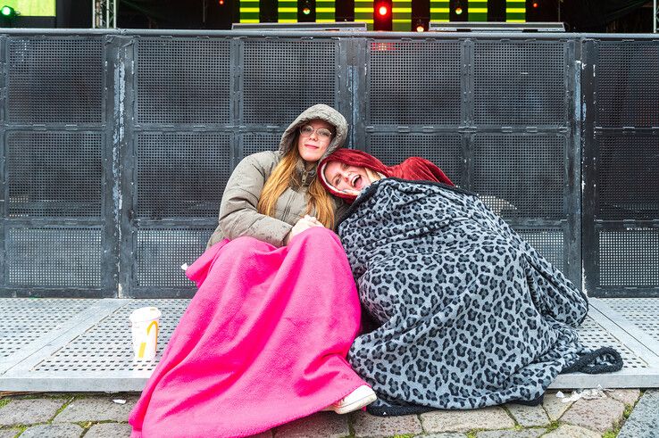 Fleur (links) en Amber (rechts) houden zich warm onder dekens bij het podium op het Rodetorenplein. - Foto: Peter Denekamp