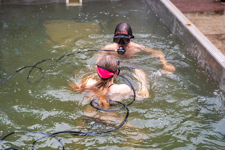 Vader en dochter met de ademautomaten en lange slangen in de dampende bak warm water. - Foto: Peter Denekamp