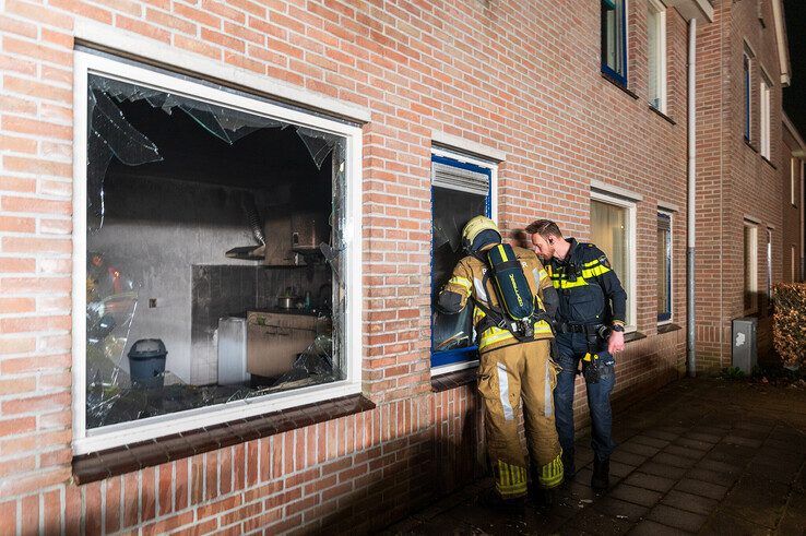 Een brandweerman en politieagent bekijken de schade in de uitgebrande keuken. - Foto: Peter Denekamp