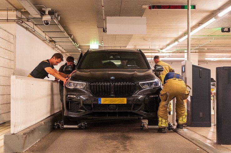 Brandweerlieden halen de naar brand stinkende auto uit de parkeergarage.