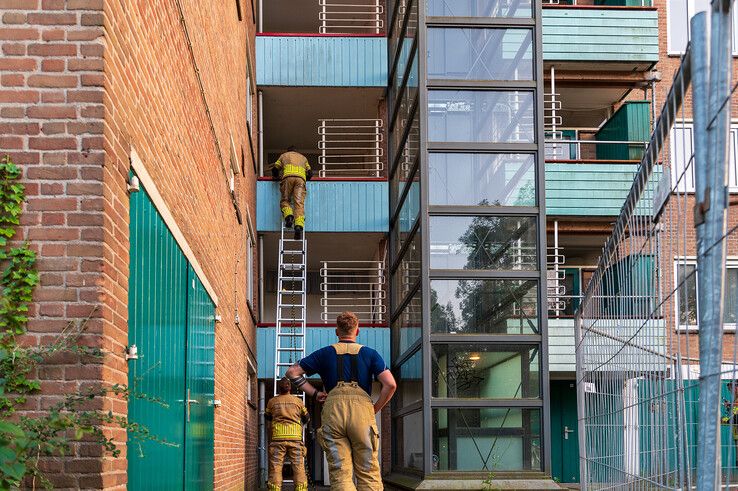 Een brandweerman klimt omhoog om de balkondeur te sluiten.