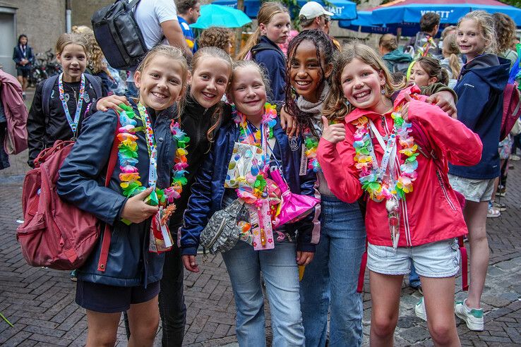 Lachende kinderen met bloemenkransen en medailles tijdens de slotavond van de Avondvierdaagse in Zwolle.