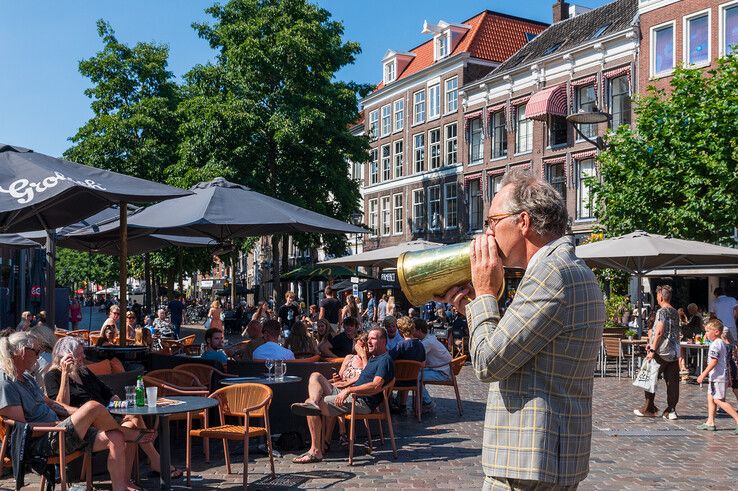 Man met koperen roeptoeter loopt langs volle terrassen op de Grote Markt in Zwolle.