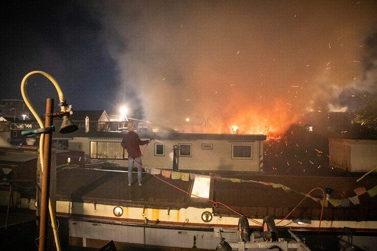Man houdt met tuinslang boot nat terwijl schuur in lichterlaaie staat.
